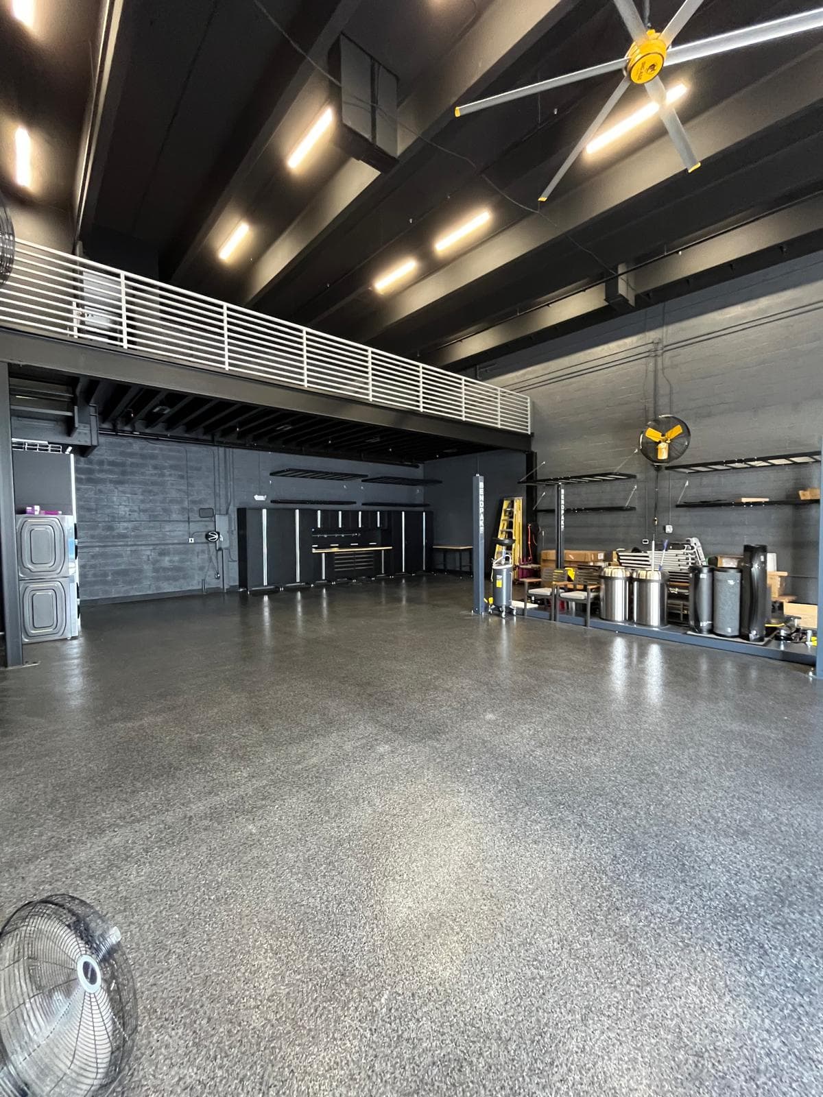 Finished workshop bay with polished speckled concrete floor, black ceiling, large HVAC fans and a white mezzanine railing
